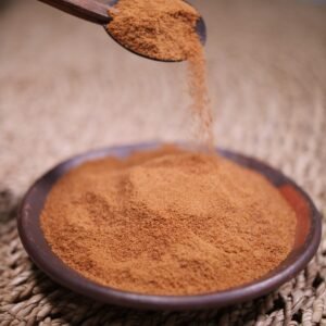 A close-up of cinnamon powder being poured from a spoon into a rustic wooden bowl, ideal for recipes.